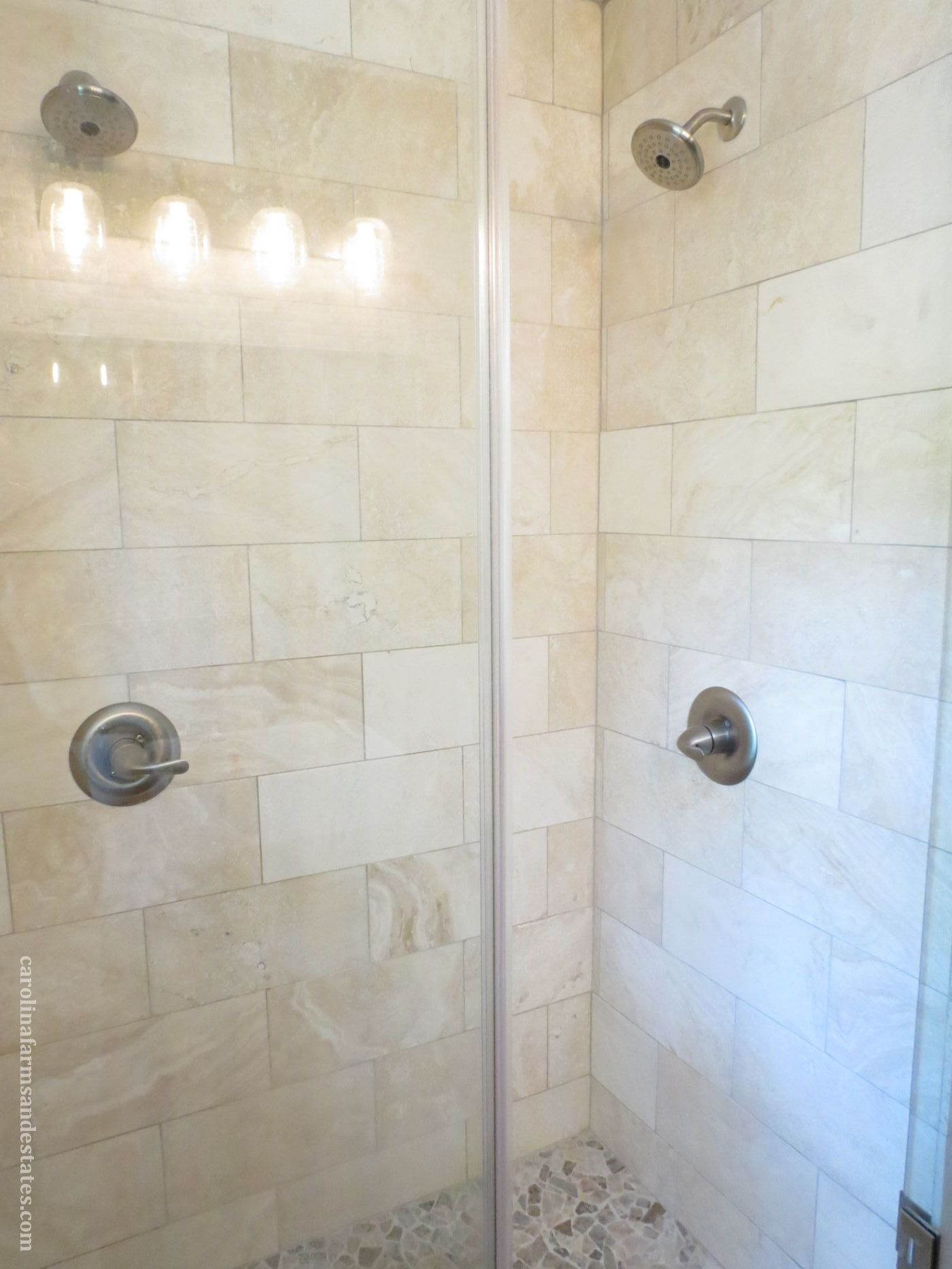 Master bath has dual-head shower, travertine tile and pebble-like floor.